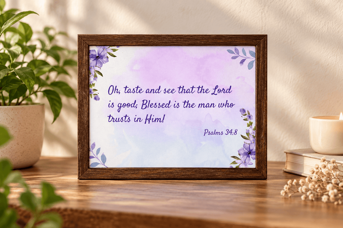 A framed Bible verse print featuring Psalm 34:8 with purple text and floral corner accents, displayed on a wooden table in a styled home setting with a plant, candle, and books.
